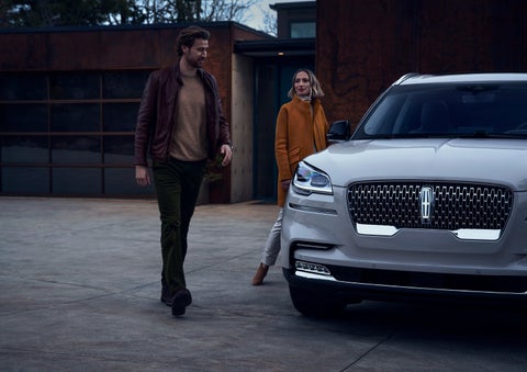 A man and a woman approaching a 2024 Lincoln Aviator® SUV, which illuminates certain lights when they are close | Ed Morse Lincoln in Muscatine IA
